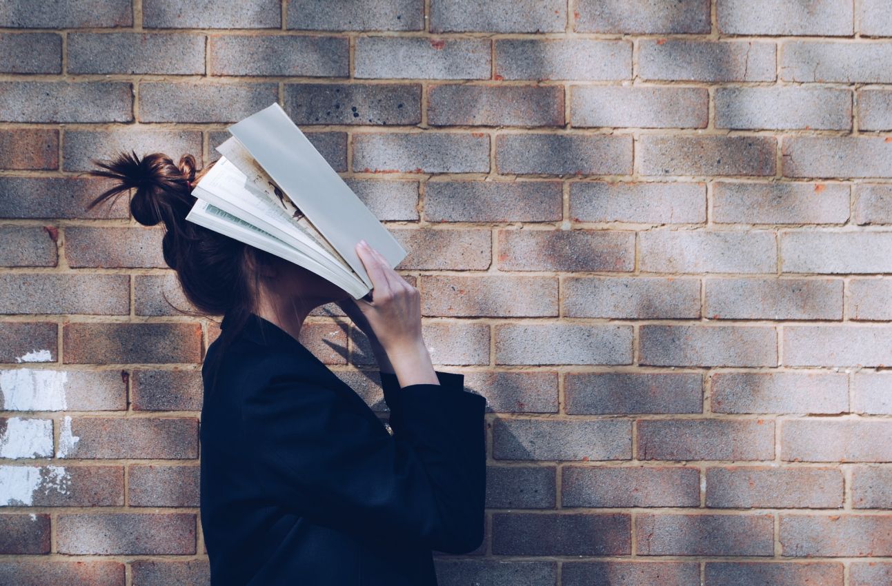 Junge Frau, die ihr Gesicht mit einem Buch verdeckt