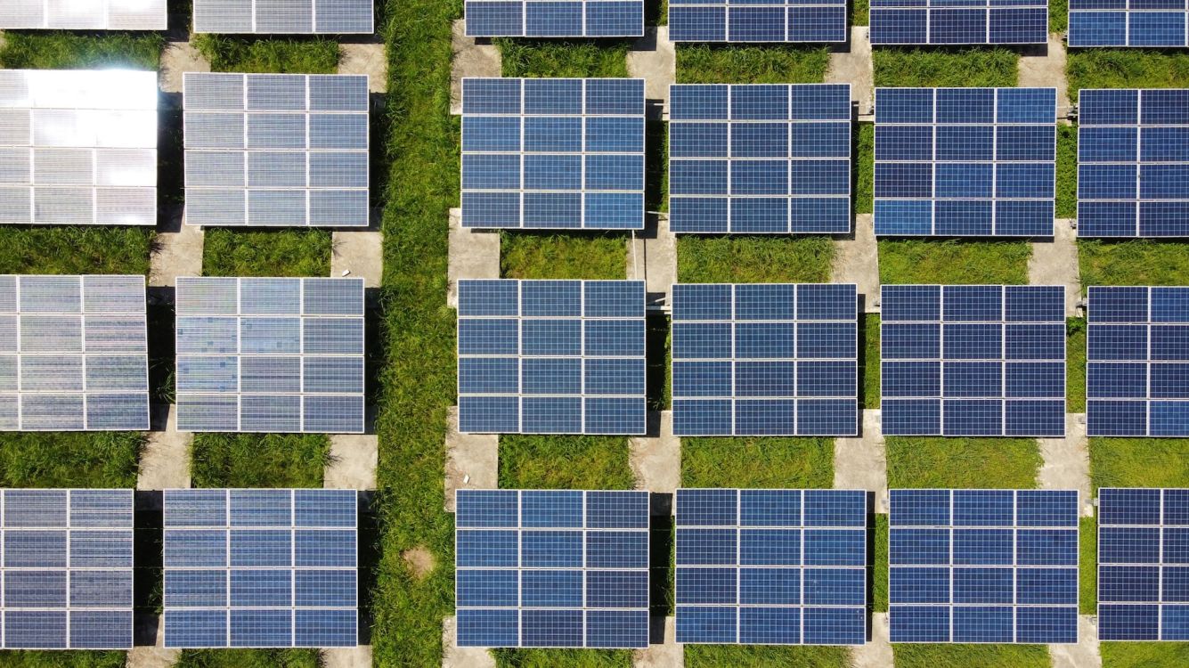 Großes Feld an Solarpanels auf grüner Wiese von oben fotografiert.