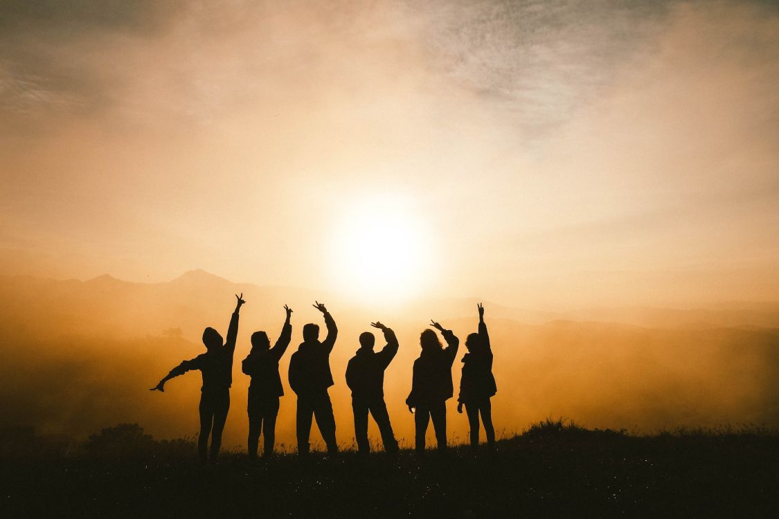 Gruppe sich freuender Menschen von hinten vor Sonnenuntergang