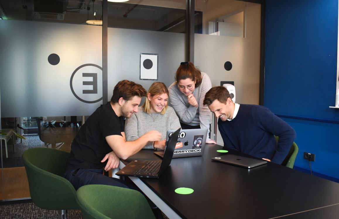 Gruppe l&auml;chelnder Menschen in einem Konferenzraum, die gemeinsam auf einen Laptop-Bildschirm schauen