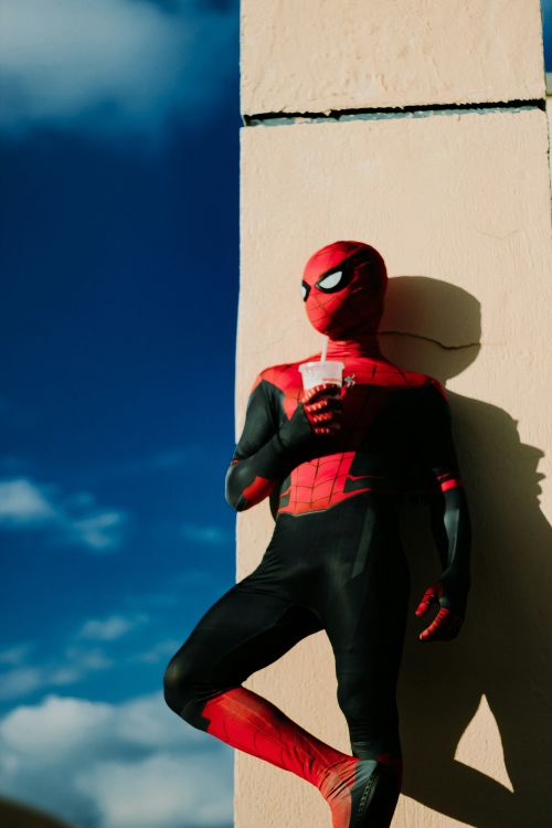 Person im Spiderman-Kostüm, der lässig gegen eine Hauswand lehnt.