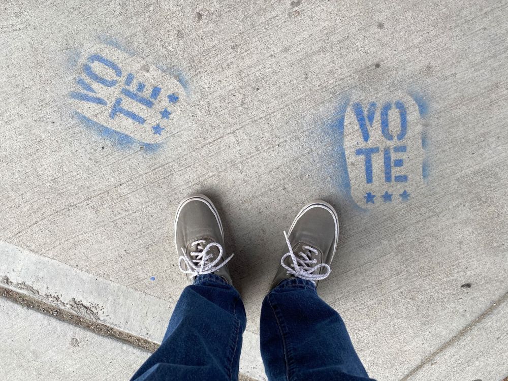 Person in Jeans und Sneakers steht zwischen zwei blauen Schriftz&uuml;gen mit dem Wort 