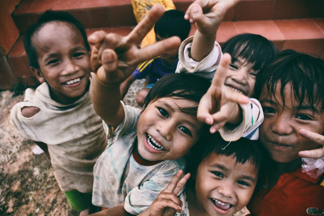 F&uuml;nf l&auml;chelnde Kinder, die ein V Friedenszeichen mit ihren Fingern formen