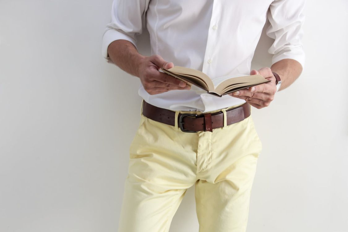 Mann im wei&szlig;en Hemd und gelber Hose h&auml;lt aufgeschlagenes Buch in den H&auml;nden