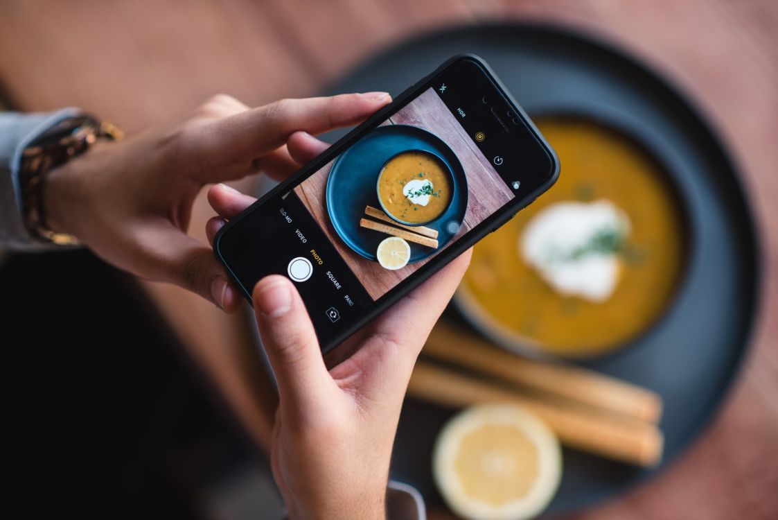 Jemand macht mit dem Handy ein Foto von einer orange-farbigen Suppe
