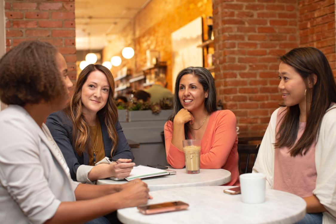 Vier Frauen sitzen zusammen in einem Caf&eacute; und unterhalten sich.
