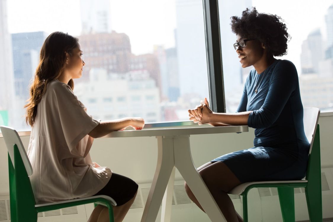zwei Frauen sitzen sich an einem Tisch gegen&uuml;ber