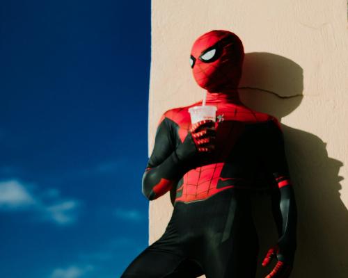 Person im Spiderman-Kostüm, der lässig gegen eine Hauswand lehnt.
