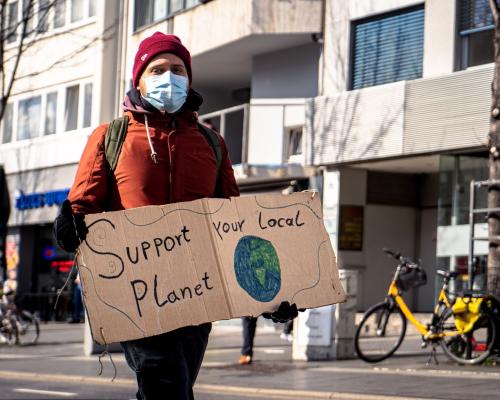 Junger Mann mit einem Schild in der Hand, auf dem steht "Support your local planet".