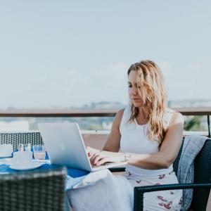 Frau, die auf einem Balkon an einem Laptop arbeitet.
